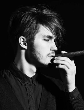 Ciddi sakallı bir adam siyah stüdyo arka planında puro içiyor.