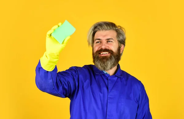 春の清掃サービス。スポンジで洗浄します。夫はきれいな家だ。衛生と純度。髭の男はゴム手袋をしてる。均一な黄色の背景の成熟した管理人 — ストック写真