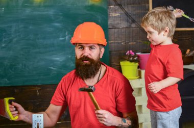 Çocuk neşeli oyunlar ve babayla alet kullanmayı öğreniyor. Baba, koruyucu başlıklı sakallı bir ebeveyn küçük oğluna okulda farklı aletler kullanmayı öğretiyor. Babalık kavramı.