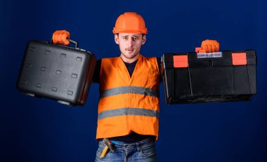 Alet çantası ve ekipman konsepti. Kasklı bir adam, içinde mavi arka plan olan alet çantası ve alet çantası olan bir şapka. Çalışan, tamirci, tamirci, düşünceli yüz yapıcı iş için ekipman seçen.