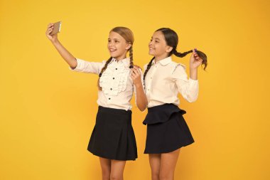 Bir selfie daha. Mutlu öğrenciler sarı arka planda akıllı telefonla selfie çekiyorlar. Cep telefonuyla selfie kameraya gülümseyen küçük kızlar. 1 Eylül'de selfie oturumu keyfi