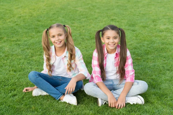 Дети это будущее. Маленькие дети сидят на зеленой траве. Счастливые дети веселятся на открытом воздухе. Маленькие дети с модным внешним видом. Тенденция случайного стиля. Счастливого детства. Международный день защиты детей — стоковое фото
