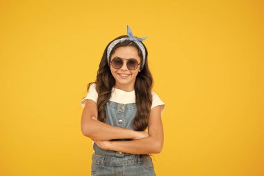 Güneşli havaya hazır olun. Yaz moda konsepti. Neşeli küçük kız sarı arka plan. Retro çocuk uzun saçlı. Küçük çocuk klasik güneş gözlüğü. Tatil modu başladı. Küçük moda ustası. Çocuk giyim mağazası.