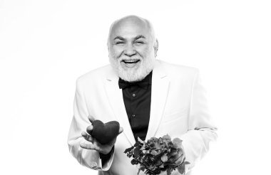 Yaşlı centilmen romantik ruh. Adam sevginin kalp sembolünü taşıyor. Yaşlılar için flört hizmetleri. Centilmen kavramı. Gerçek bir beyefendi. Yakışıklı sakallı adam smokin giyer. Romantizm ve flört