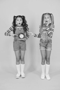 Mutlu küçük kızlar sarı arka planda klasik çalar saat bulundururlar. Küçük çocuklar mekanik saatle gülümsüyor. Okul saati. Kişisel plan ve program. Zaman kavramı sayılıyor. Ölü satır