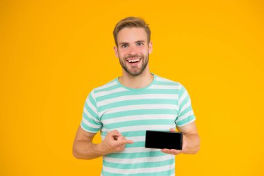 Senin için en iyi telefon. Akıllı telefonun sarı arka planına bakan mutlu adam. Reklam için işaret. İşaret parmağı. Gösterişli bir jest. En iyi seçim. Bu aslında hayatını kolaylaştıracak.