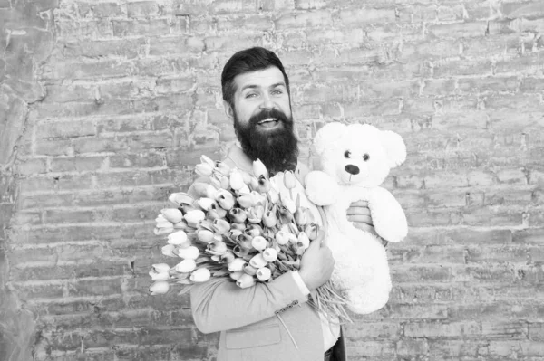 Homme porter bleu nœud papillon tuxedo tenir bouquet de fleurs. Journée internationale de la femme. La surprise va lui faire fondre le cœur. Homme romantique avec des fleurs et un ours en peluche. Cadeau romantique. Macho se préparer date romantique — Photo