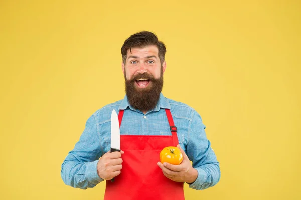 Skäggig man i rött förkläde med gul tomat. matlagning hälsosam och färsk mat. Snygg manlig kock jobbar. mogen kock skära grönsaker. Killen i uniform i köket. vitamindiet — Stockfoto