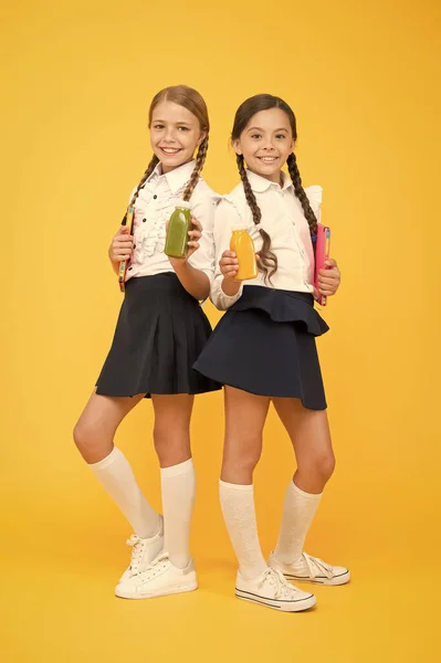 Thirst and dehydration. Healthy nutrition. Schoolgirls holding juice bottle on yellow background. Quenching thirst during school time. Healthy snack fruit smoothie. Smoothie detox. Yummy smoothie — Stock Photo, Image