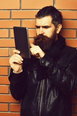 Kahverengi tuğla duvar stüdyosunun arka planında tablet tutan Kafkas hippi sakallı.