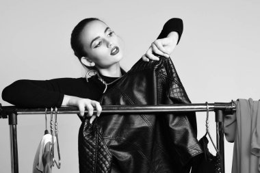 Güzel kız elbise ve askılarda siyah ceketle poz veriyor.