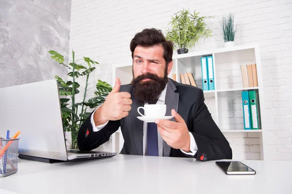 커피를 즐기는 가장 좋은 방법입니다. 수염이 많은 남자가 커피 잔 앞에 엄지손가락을 보여 주고 있다. 사업가는 사무실에서 커피를 마십니다. 커피 휴식. 따끈 한 술. 아침 차. 좋은 아침 음료. 단순 한 쾌락 — 스톡 사진