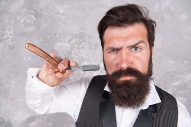 Sakallı ve şık. Retro ve klasik moda. Saç ve sakal bakımı. Kendine güvenen ve yakışıklı vahşi bir adam. Erkek sabah bakımı. Kişisel yüz bakımı. Tıraş eden adamın jileti var. Erkekler için kuaför salonu