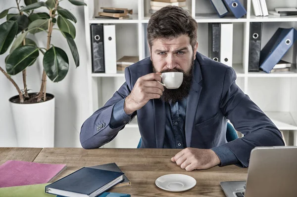 피곤 한 남자는 커피를 마신다. 에너지가 더 필요 합니다. 이른 아침 술. 현대 사무실 생활. 직장에서의 성숙 한 사업가. 심한 노동으로 지친 상태에서. 시오는 노트북과 노트북을 가지고 탁자에 앉아 있다 — 스톡 사진
