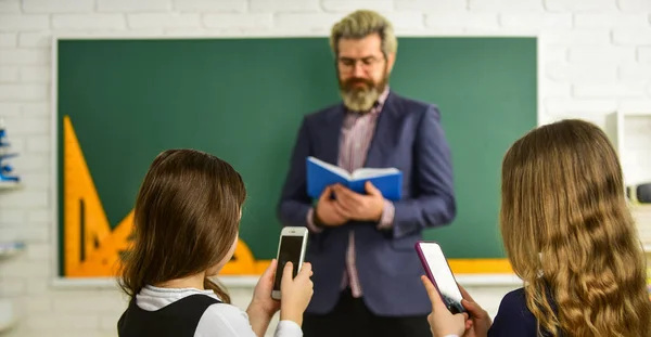 Problema de los teléfonos inteligentes en las escuelas. Diviértete con el teléfono inteligente en lugar de estudiar. Adicción a Internet. Adicta a los juegos en línea de Internet. Navegar por Internet en las redes sociales. Estudiantes de escuela y profesor —  Fotos de Stock