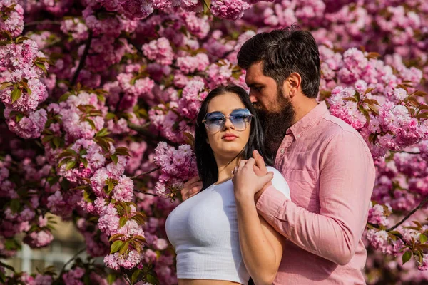 Casal na moda em fundo de primavera. Casal apaixonado apreciando flor de cereja rosa. Homem e mulher no jardim florescente. Feliz Páscoa. casal no amor sakura flor. homem e mulher em flor de cereja — Fotografia de Stock