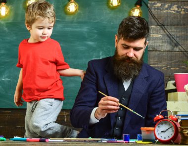 Aile meşgul yüzler yaratıyor, çiziyor. Ders çizimi konsepti. Baba ve oğul çalışma odasında birlikte resim yapıyorlar. Öğretmen ve çocuk arka planda kara tahtayla sınıfta..