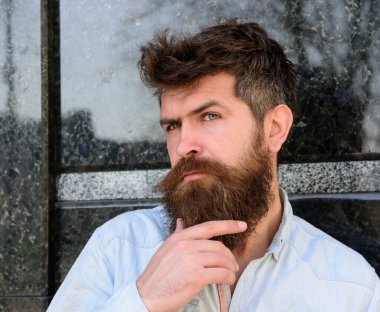 Sakallı, bıyıklı, düşünceli, siyah mermer arka planda bir adam. Erkeklik kavramı. Kıvırcık saçlı hippi uzaktan bakarken sakala dokunuyor. Adam meraklı ve meraklı görünüyor..