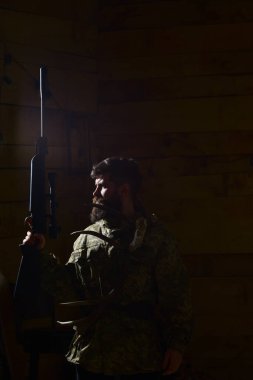 Avcı konsepti Sakallı bir adam kamuflaj kıyafeti giyiyor, koyu bir geçmişi var. Geyik boynuzları ve silahla vahşi bir avcı karanlıkta parlıyor. Avcı evinde avlanmaya hazır sert suratlı maço..