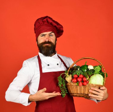 Katı yüzlü, bordo üniformalı aşçı sebze sunar
