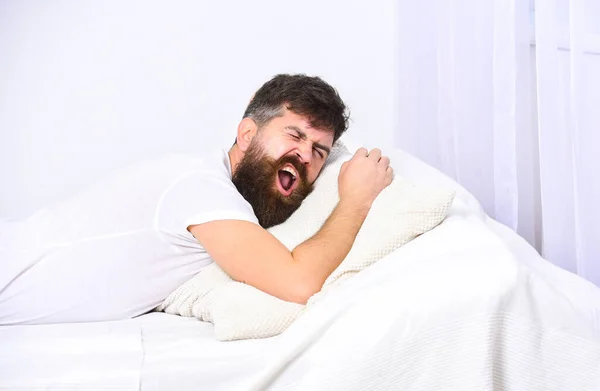 Hombre de camisa acostado en la cama, pared blanca en el fondo. Concepto siesta y siesta. Un tipo con la cara cansada y soñolienta bostezando. Macho con barba y bigote bostezando, relajándose, durmiendo la siesta, descansando . — Foto de Stock