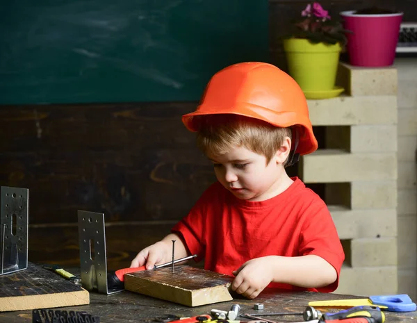 Egy srác narancssárga keménykalapban vagy sisakban, tanulószoba háttér. Gyerekkori koncepció. Fiú játszani, mint építész vagy javító, dolgozni szerszámok. Gyermek álmodik jövőbeli karrierjét az építészet vagy az épület. — Stock Fotó