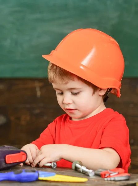 Bambino sul viso occupato gioca con bulloni a casa in officina. Il ragazzo gioca come tuttofare. Bambino in cappello rigido, casco che gioca con bulloni esagonali come costruttore o riparatore, artigianale. Concetto artigianale . — Foto Stock