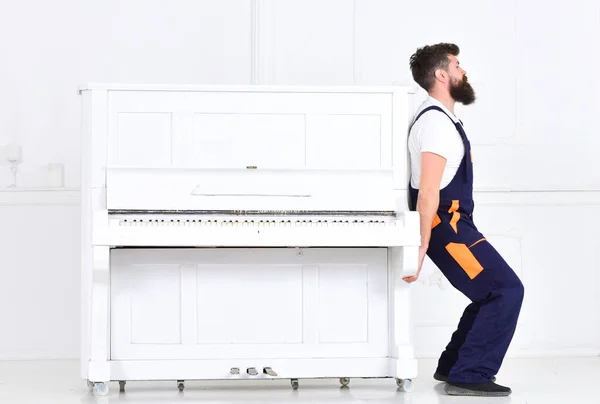Guapo barbudo hombre fuerte levantando viejo piano de madera con teclado abierto aislado sobre fondo blanco. Vista lateral trabajador guapo tratando de mover cosa pesada —  Fotos de Stock