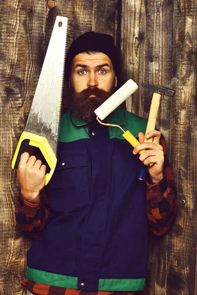 Бородатый строитель держит различные строительные инструменты с удивленным лицом — стоковое фото