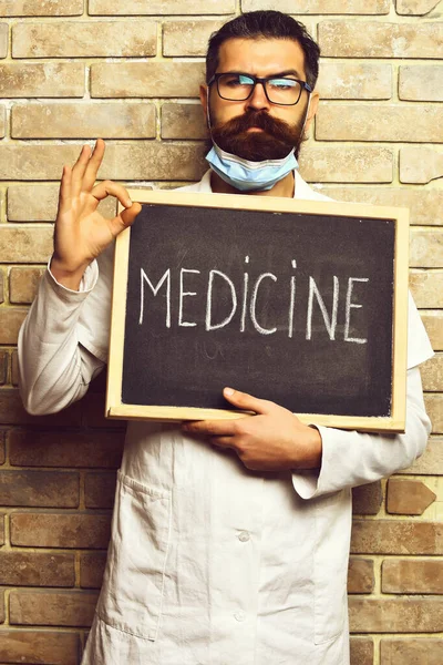 Brutalny, biały lekarz trzymający tablicę z napisem "Medycyna" na beżowym ceglanym tle studia — Zdjęcie stockowe