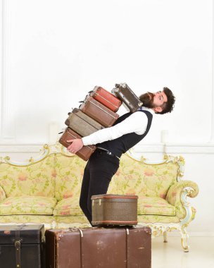 Bıyıklı ve sakallı bir adam klasik takım elbise giyiyor. Bavul teslim ediyor. Beyaz, lüks bir iç mekan. Uşak ve servis konsepti. Maço, zarif hamal ağır antika bavullar taşıyor.