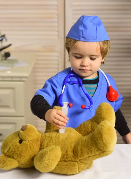 Niño en uniforme quirúrgico sostiene jeringa sobre fondo de madera. —  Fotos de Stock