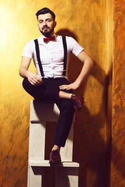 Sakallı adam ciddi yüzüyle sandalyede oturuyor.