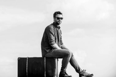 Gezgin, uçuşu bekle. Çekil şuradan. Maço, tıraşsız bir adam tur çantasına oturur. Erkek modası. Çok modaya uygun görünüyorsun. Gözlüklü iş adamı. İş gezisi. Seksi erkek gökyüzü arka planı. Kalacak yer ara