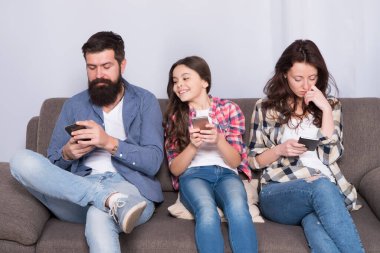 Anne baba ve kızı kanepede dinleniyor. Aile hafta sonunu internette geçiriyor. Küçük bir kız çocuğu, ailesine karşı akıllı telefon kullanıyor. İnternette aile sörfü. Aile eğlencesi. Oyun uygulaması oynat. Çevrimiçi aile