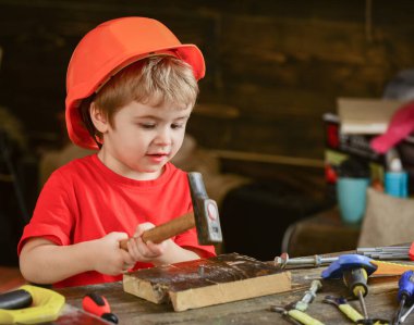 Küçük çocuk tahta tahtaya çivi çakıyor. Tozlu çalışma masasında oturan sevimli çocuk. Aletlerle çalışan konsantre bir çocuk.