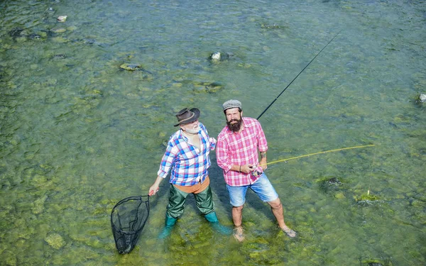 共有することです。父と息子の釣り。趣味とスポーツ活動。トラウト・ベイト。男性の友情。家族の絆。釣竿と網を持った2人の幸せな漁師。夏の週末。成熟した男性漁業者 — ストック写真