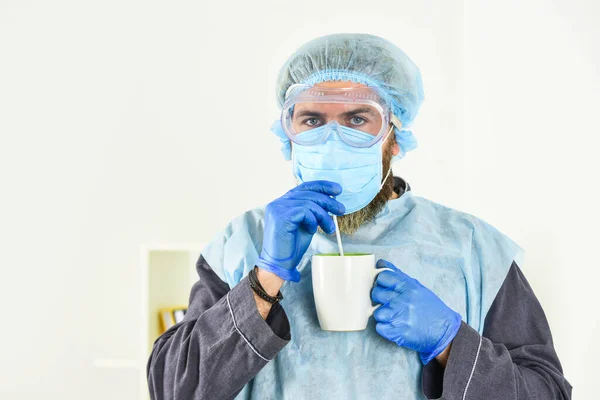 Garments placed to protect health. Face protection goggles mask gloves head cover. Personal protective equipment. Guy in mask drink tea coffee using straw. Infection prevention and control measures