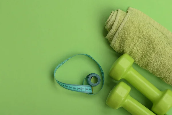 Dumbbells in green color, twisted measure tape and towel