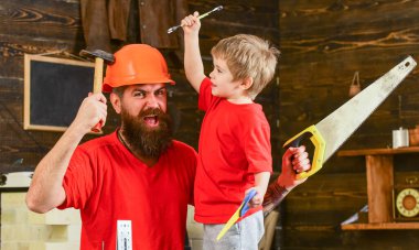 Babalık kavramı. Neşeli çocuk İngiliz anahtarı tutuyor, babayla alet kullanmayı öğreniyor. Baba, koruyucu başlıklı sakallı bir ebeveyn küçük oğluna okulda farklı aletler kullanmayı öğretiyor..