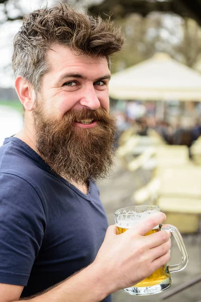 Mężczyzna z brodą i wąsami trzyma szklankę z piwem podczas relaksu na tarasie kawiarni. Szczęśliwy uśmiechnięty młodzieniec pijący piwo w barze na świeżym powietrzu w lecie. Koncepcja piwa zanurzeniowego. — Zdjęcie stockowe