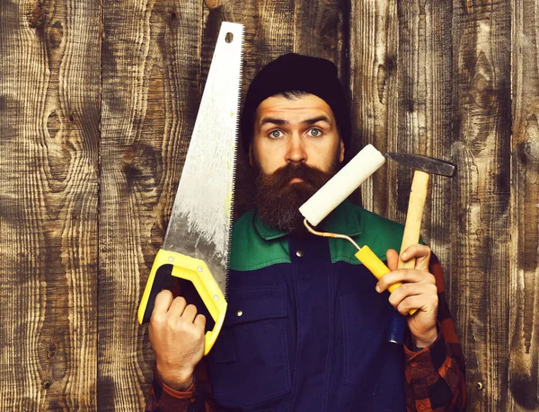Homem barbudo segurando várias ferramentas de construção com rosto surpreso — Fotografia de Stock