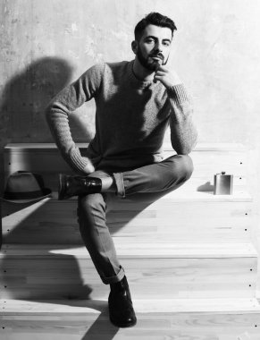 Sakallı adam merdivenlerde oturuyor, ciddi bir yüzü var.