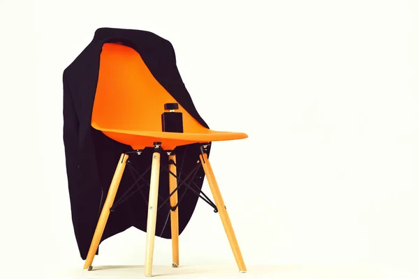 Silla de oficina de plástico naranja con chaqueta negra y frasco de perfume —  Fotos de Stock