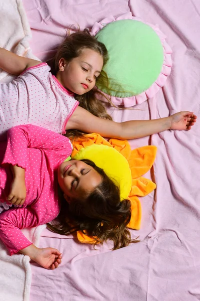 Schoolgirls in pink pajamas sleep on colorful pillows, top view