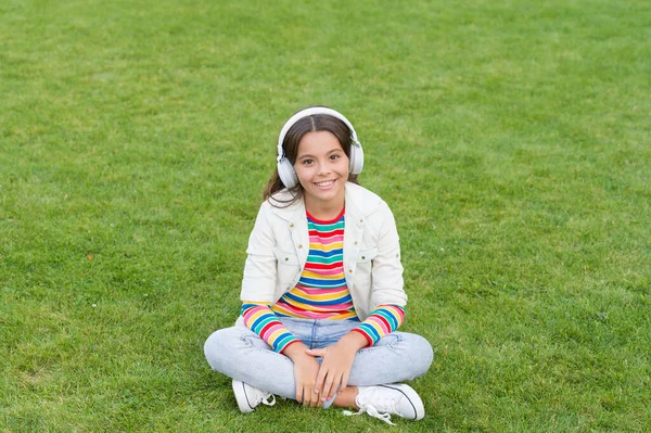 feeling carefree. small kid in headphones. summer playlist. enjoy spring nature outdoor. child study audio book. new technology. Child listen music on grass. Healthy lifestyle and relax. Yoga girl