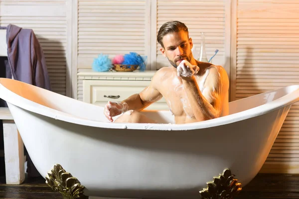 Macho sitzt nackt in Badewanne und bläst Schaum aus der Hand — Stockfoto