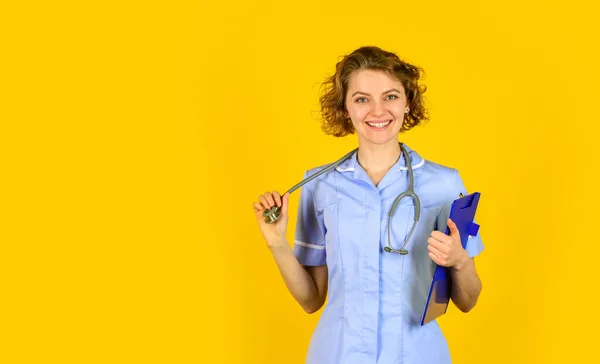 Χαρούμενη νεαρή νοσοκόμα κρατώντας πρόχειρο. Οι γυναίκες γιατροί χρησιμοποιούν στηθοσκόπιο. θεραπευτής με στολή στο νοσοκομείο. ιατρικό ιστορικό και συνταγή. Επαγγελματίας γιατρός κρατάει φάκελο. αντίγραφο χώρου — Φωτογραφία Αρχείου