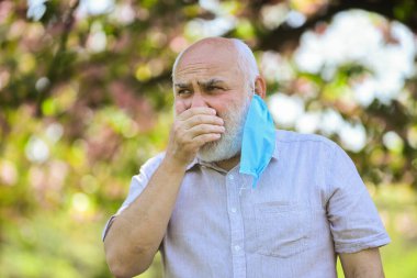 Tıp maskeli son sınıf öğrencisi öksürüyor. Parktaki çiçek ağacı. Coronavirus kapanışı sırasında hayat. Hastalık korkusu. Virüsle savaşma stratejisi. Halka açık yerlerde ziyaret yasağı