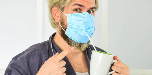 Serieus over hygiëne. Een gemaskerde man drinkt thee met stro. Bedek mond en neus met masker en zorg ervoor dat er geen gaten tussen gezicht en masker. Helemaal beschermd. Draag masker te beschermen tegen coronavirus — Stockfoto